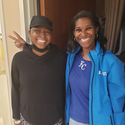 Vanessa smiles while standing with a friend, giving a peace sign with their fingers.