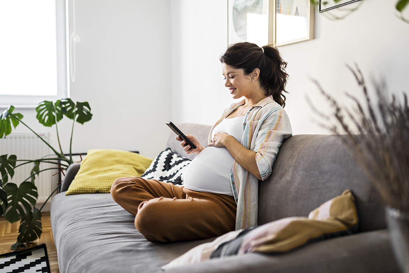 An expectant mom looks at her phone while sitting on the couch