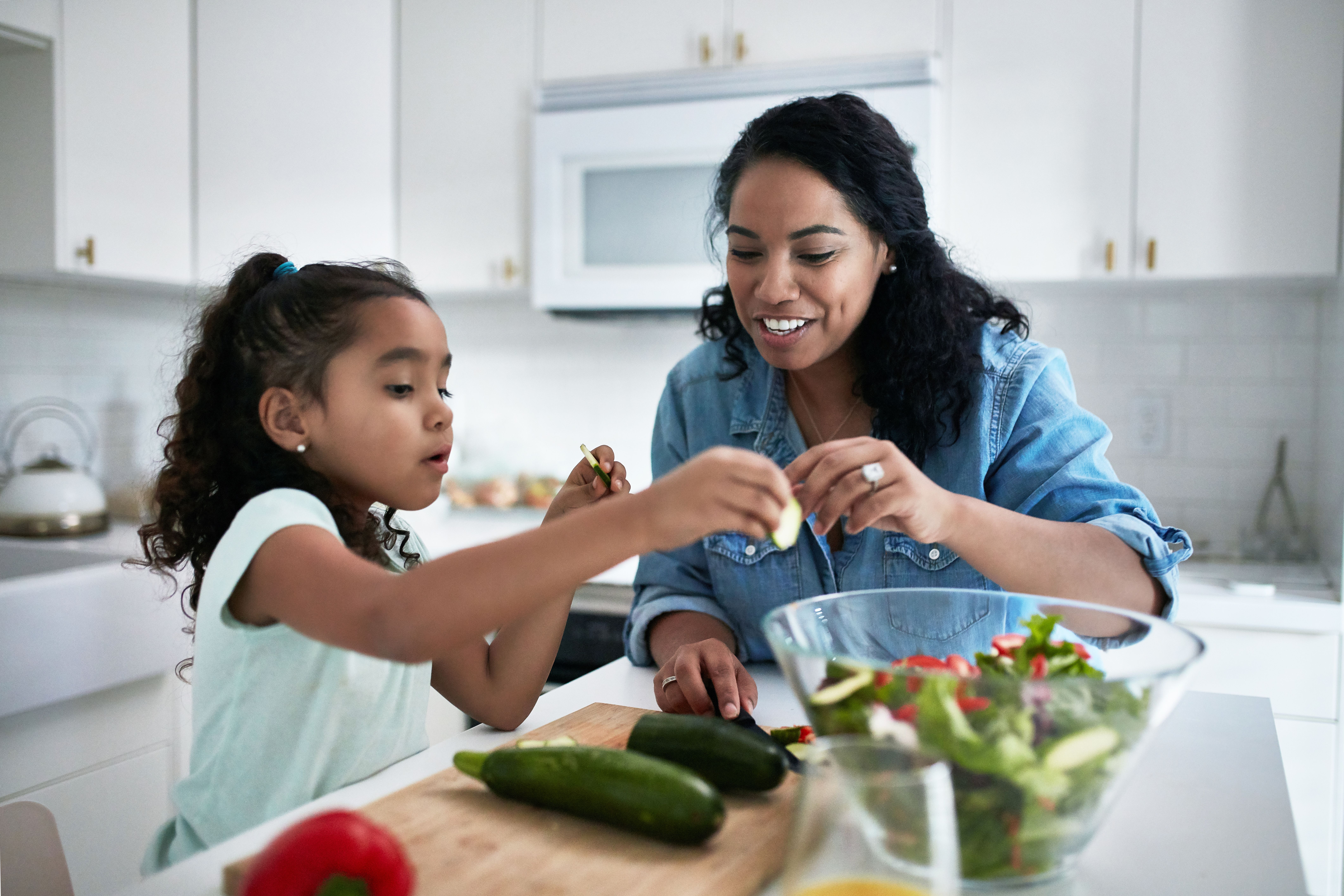 Young girl making a salad with her mother.