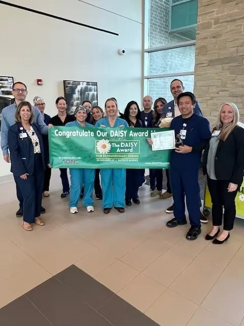 Dave Galimba with his team standing behind a large green DAISY Award banner.