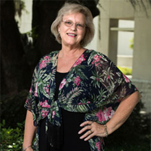 Jan Carter wearing a floral top with her hand on her hip.