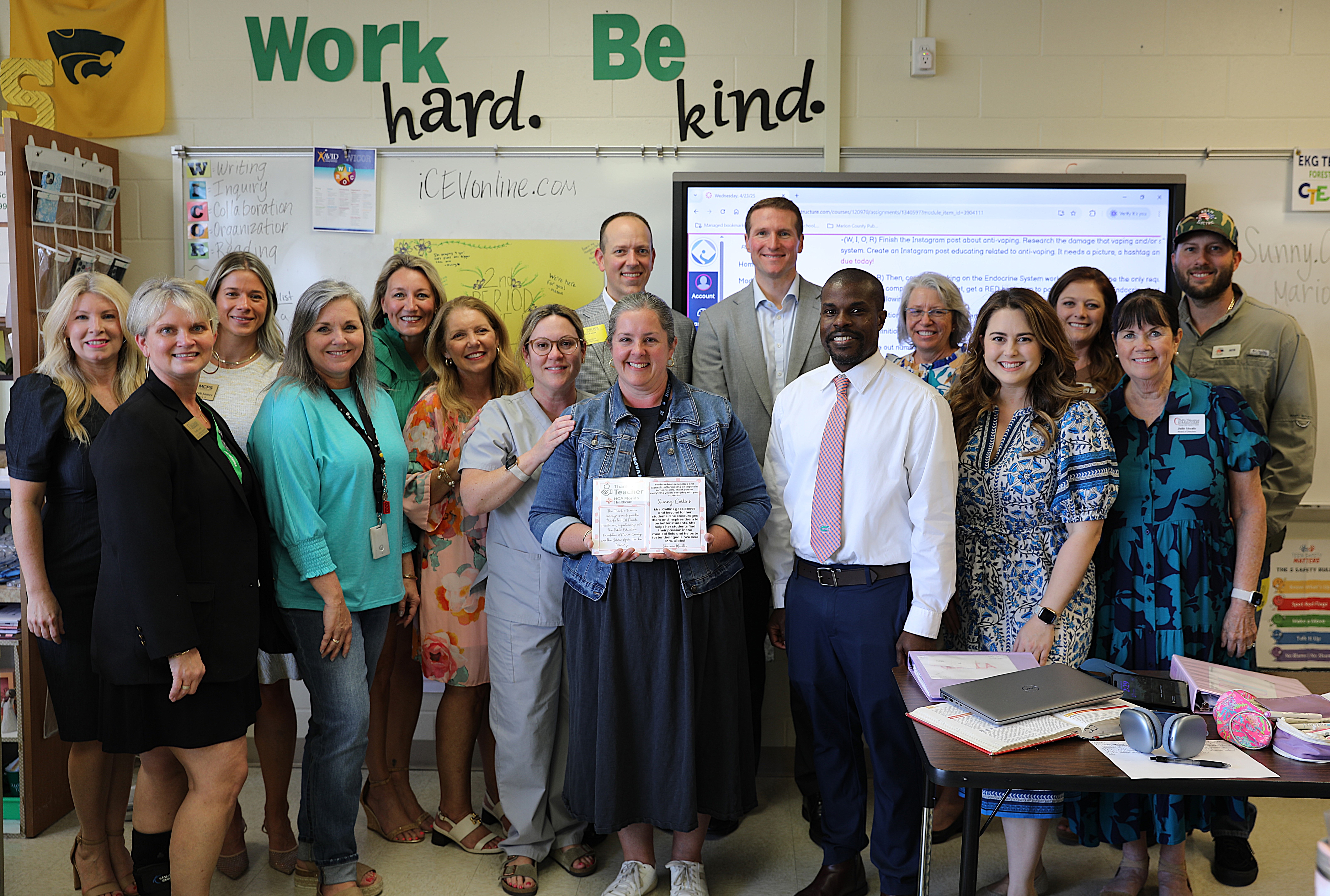 group of 4 men and 12 women smiling while in a school classroom. 
