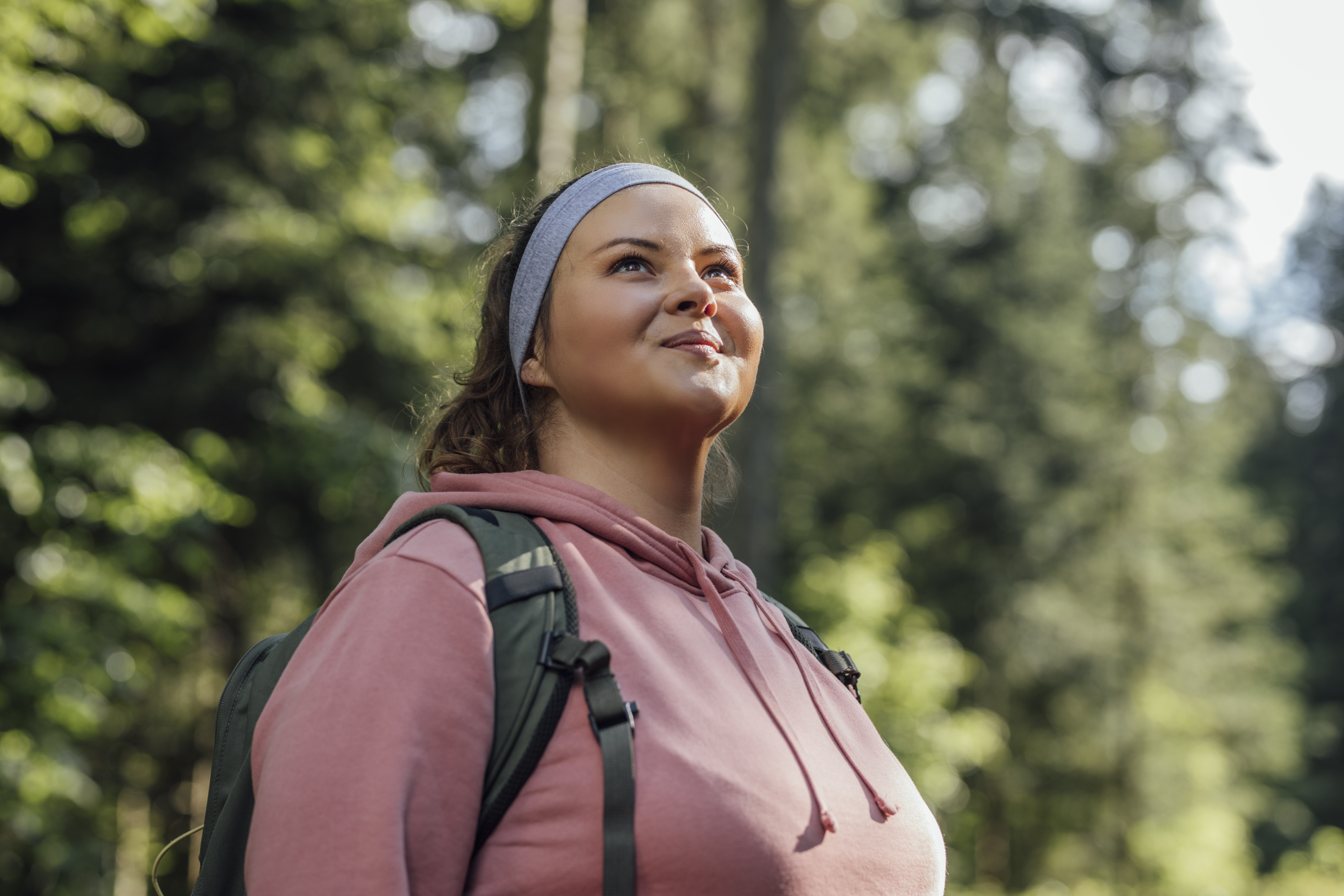 A smiling woman wearing a backpack stands in a forested area.
