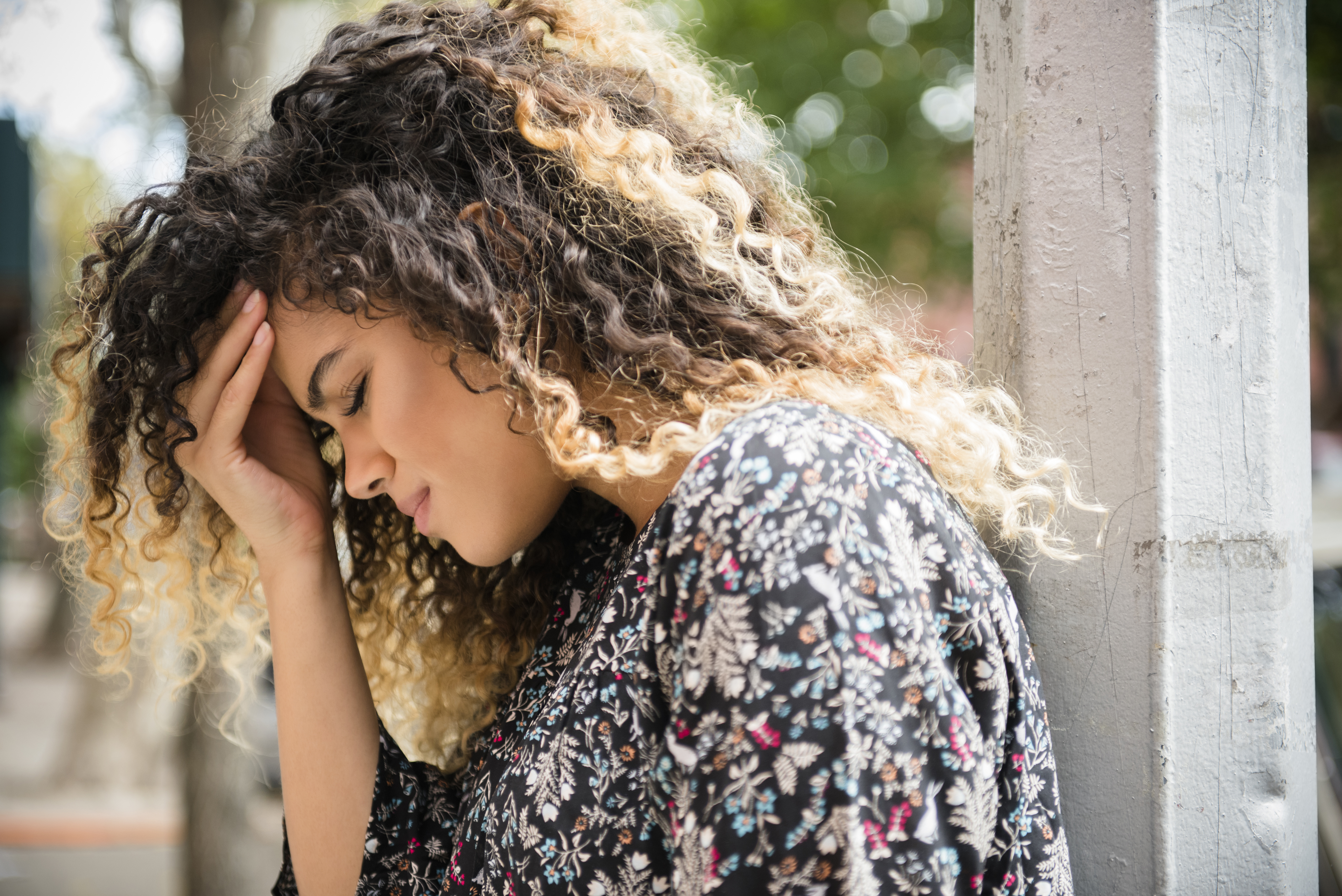 Woman with curly hair with her hand to her forehead.