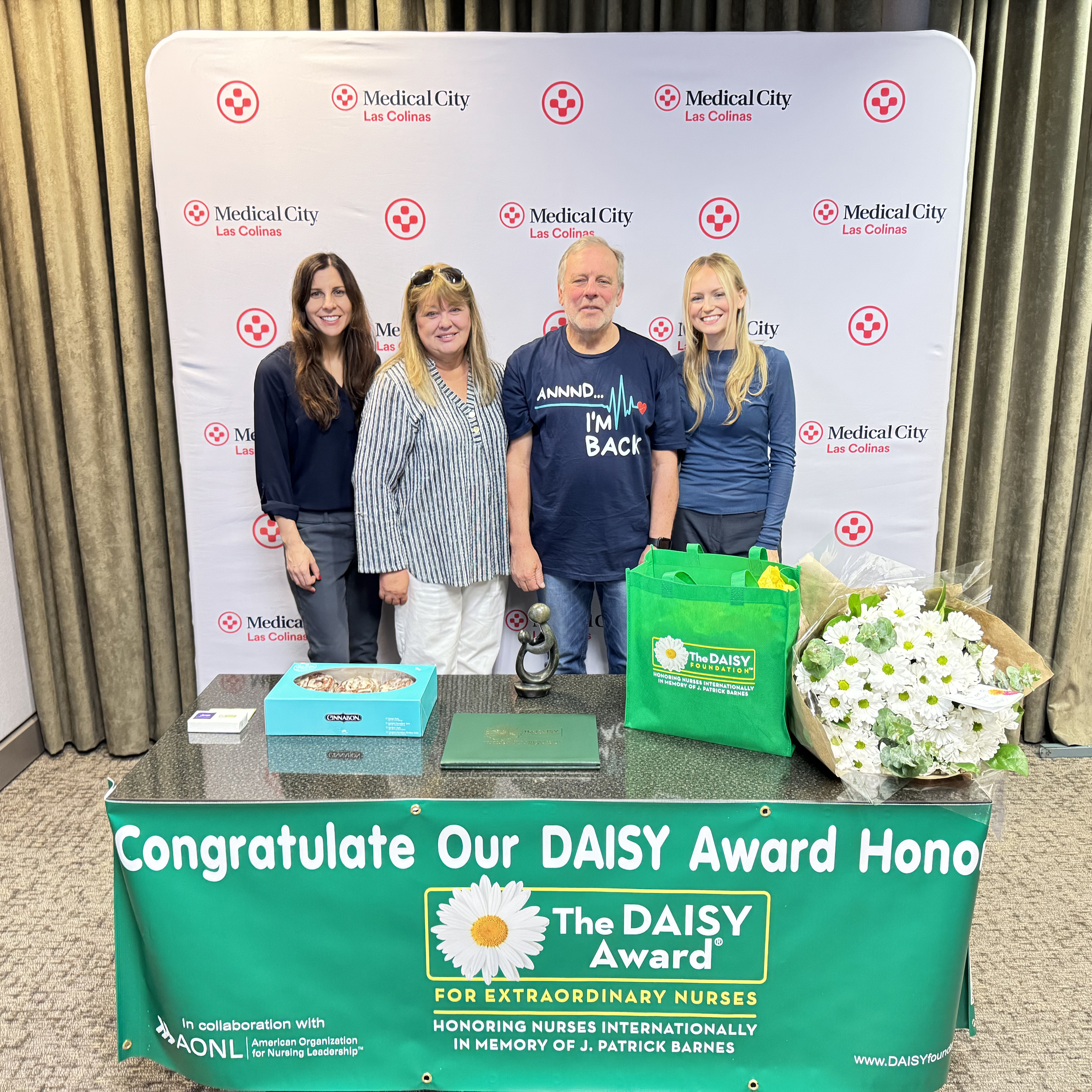 nurse Madie Wood with patient and family. table with award, flowers and cinnamon rolls