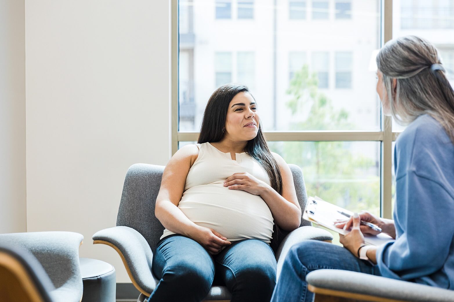A pregnant woman sitting in a waiting room talking to a nurse.
