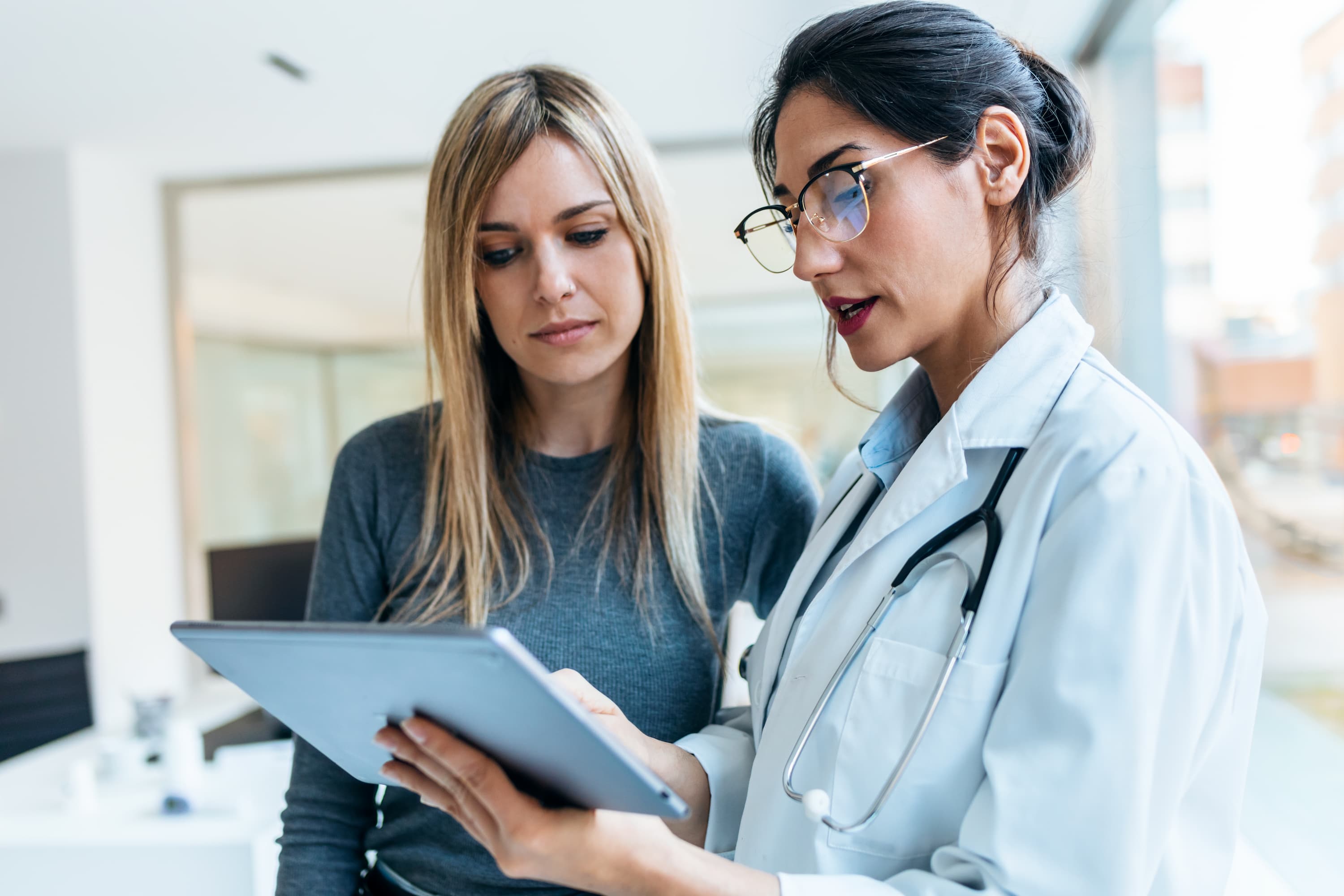 Doctor talking while explaining a medical treatment with digital tablet to patient in the consultation.