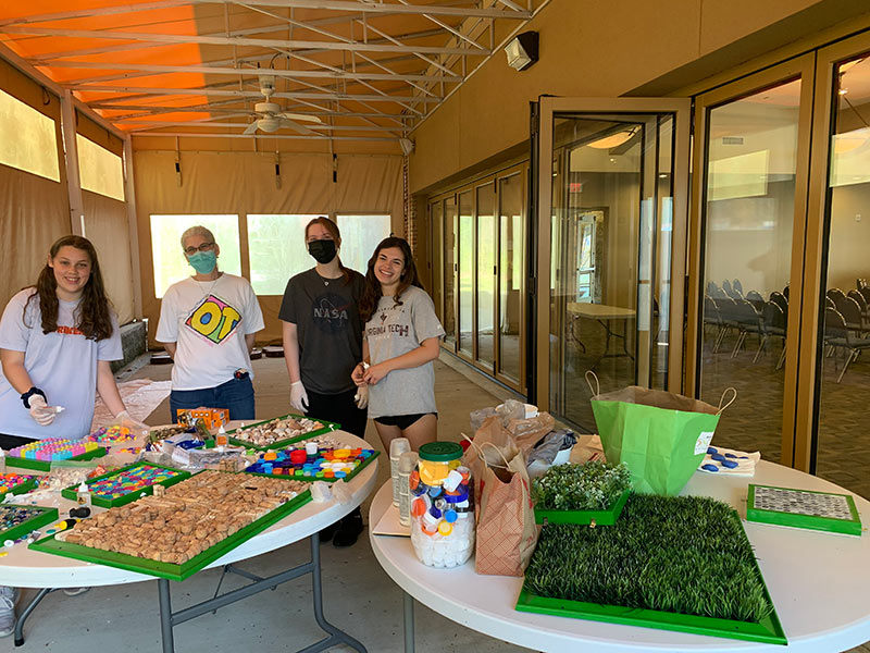 Terry Schultz poses with other volunteers in front of two tables displaying sensory aids and herbs to build the "sensory gardens."
