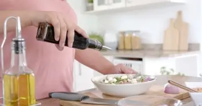 A person pouring balsamic vinegar over a bowl of salad.
