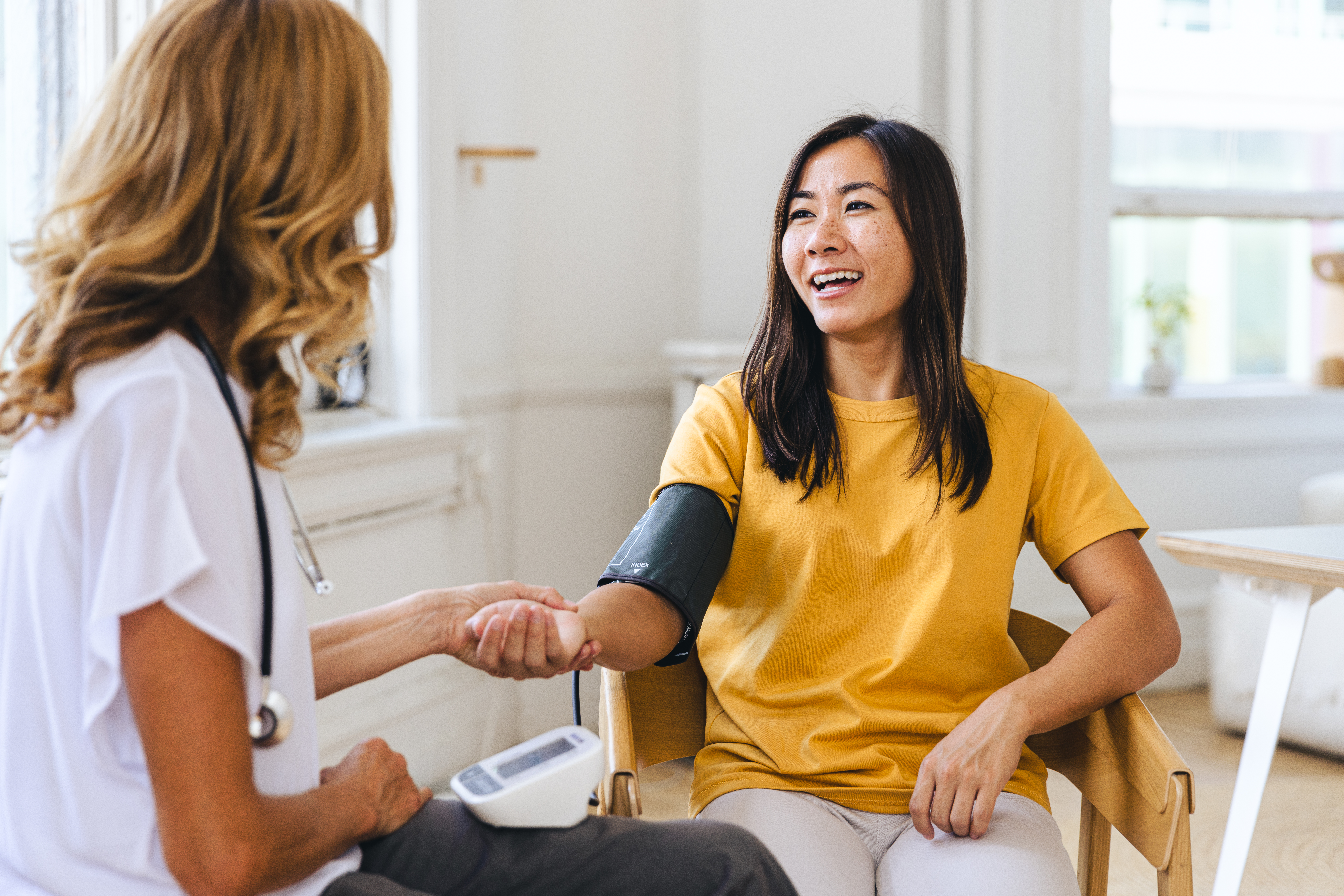 Happy female patient looking at doctor checking her pulse in hospital