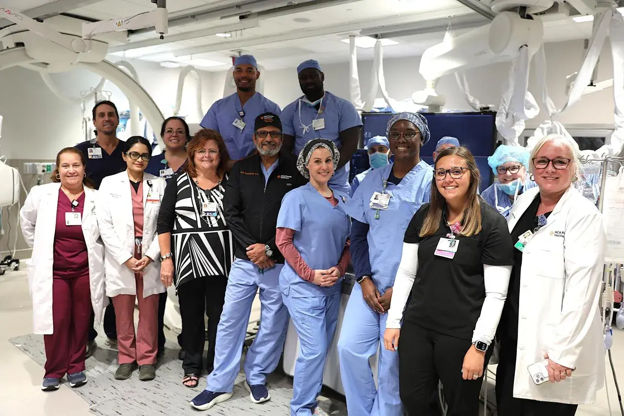 group of providers standing in operating room with surgery robots, posing for group photo