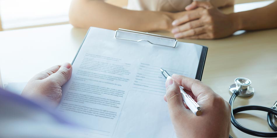 A doctor meets with a patient, reviewing a document on a clipboard.