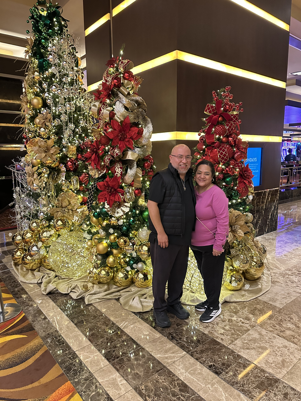 Carlos Tristan and his wife, Belinda, standing next to Christmas trees