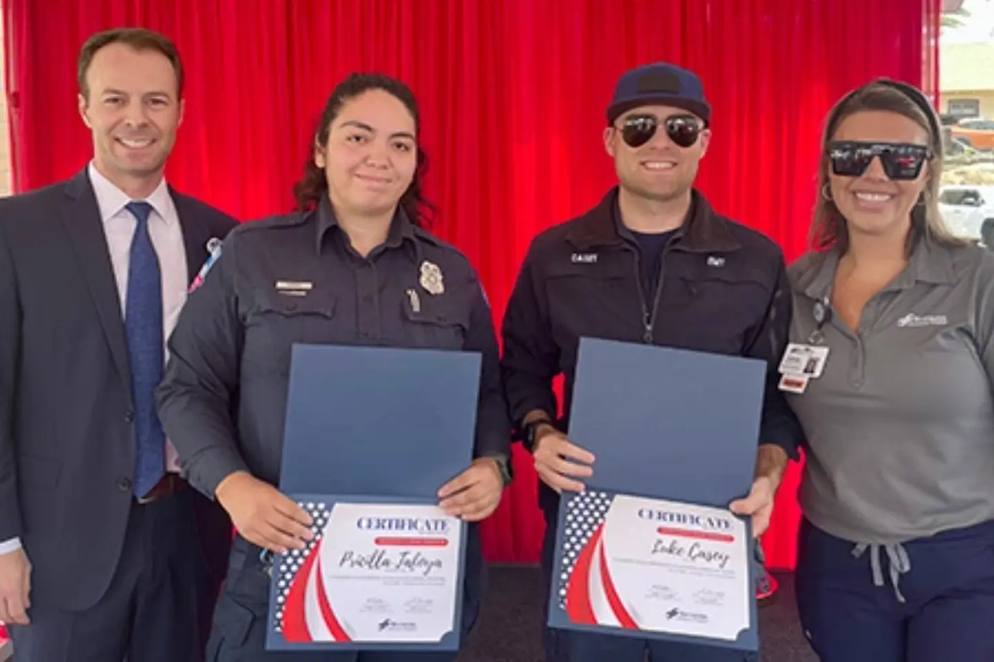AMR paramedic Pricilla T. and AMR EMT Luke C. smile while holding certificates honoring their efforts as first responders.