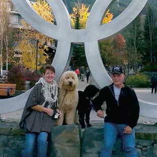 Cancer survivor Marnel Groebner smiling with pet dog and her husband outdoors.