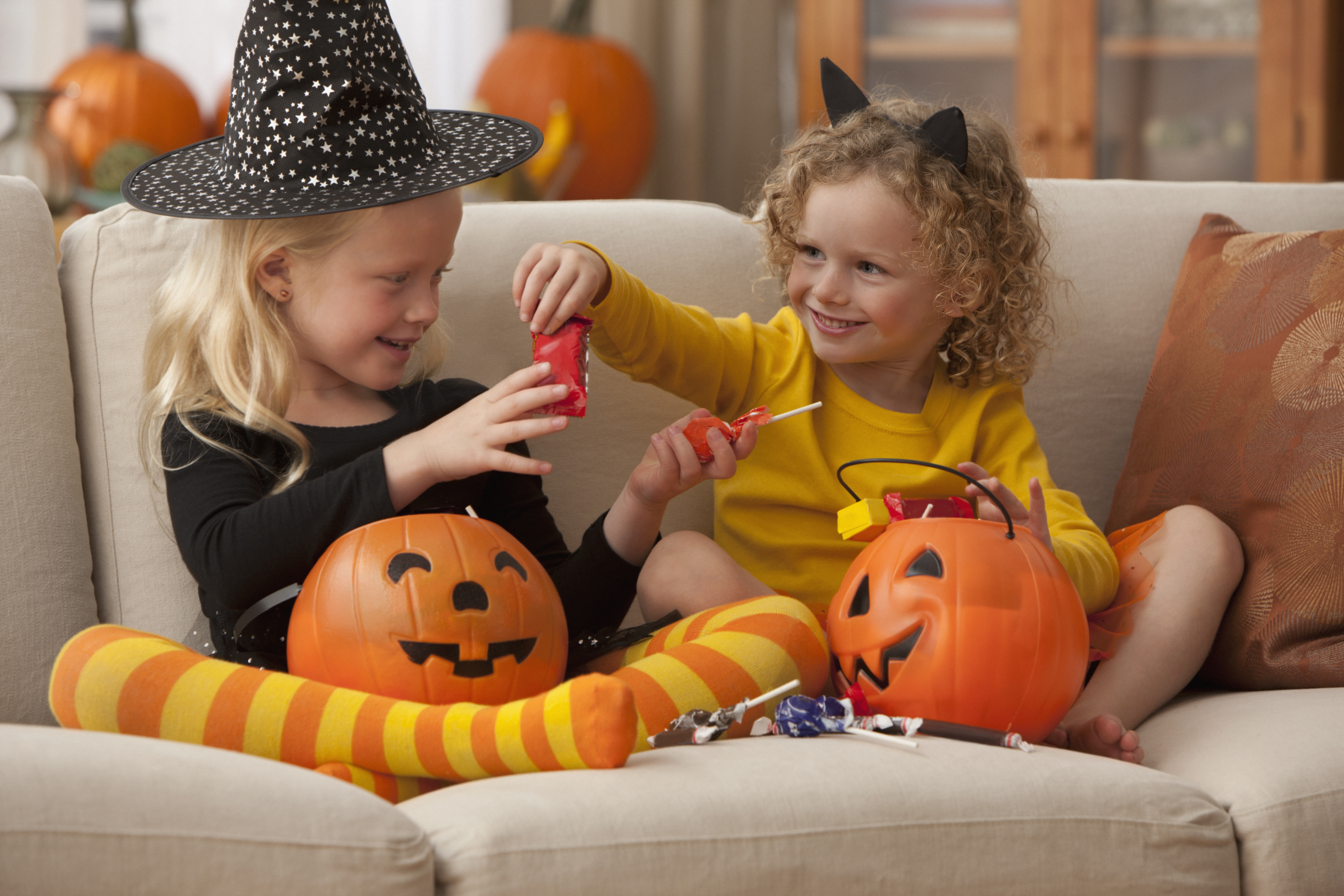 Two children in Halloween costumes exchanging candy while sitting on a couch