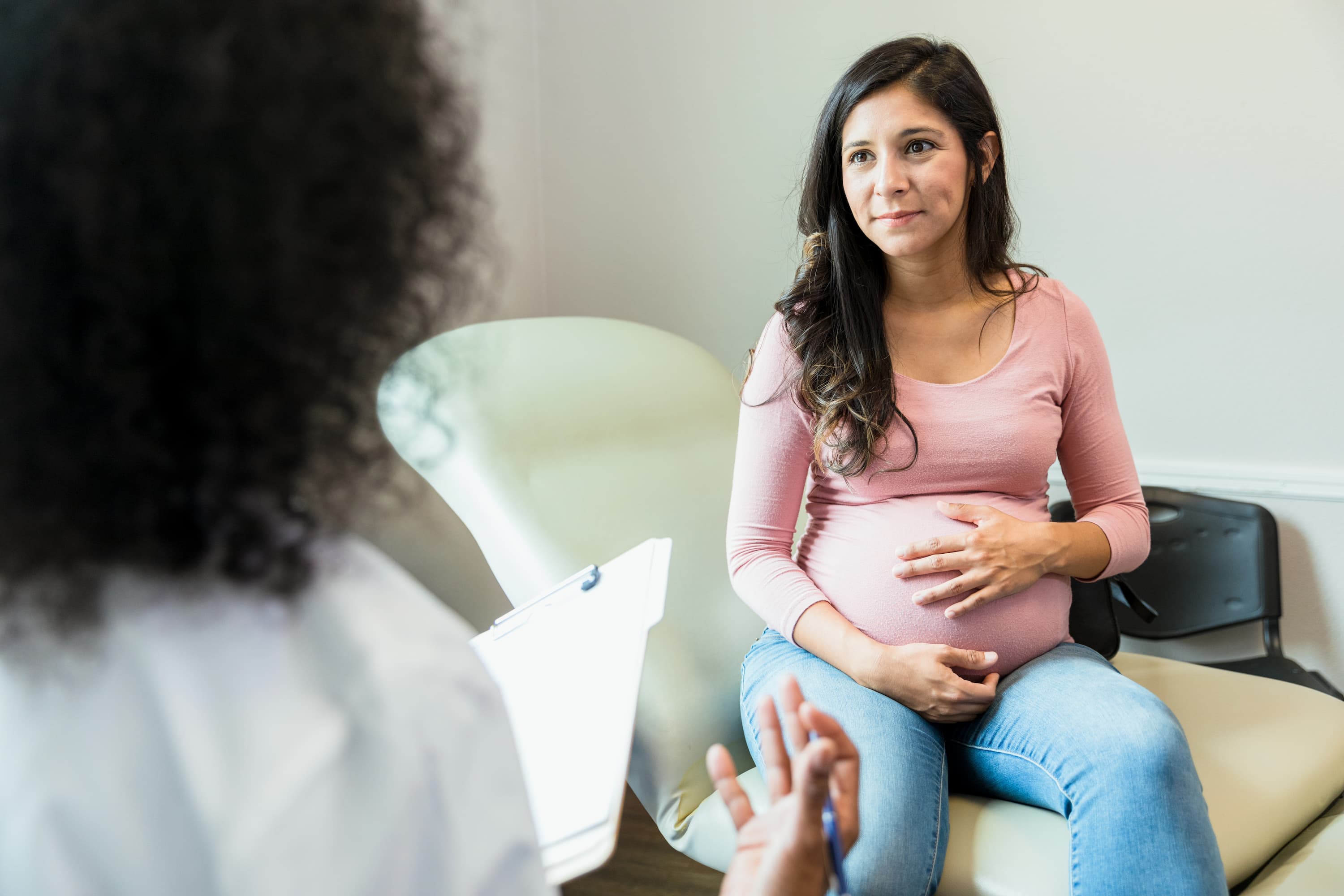 Pregnant woman sitting on an exam table and talking with a healthcare provider during a prenatal appointment.
