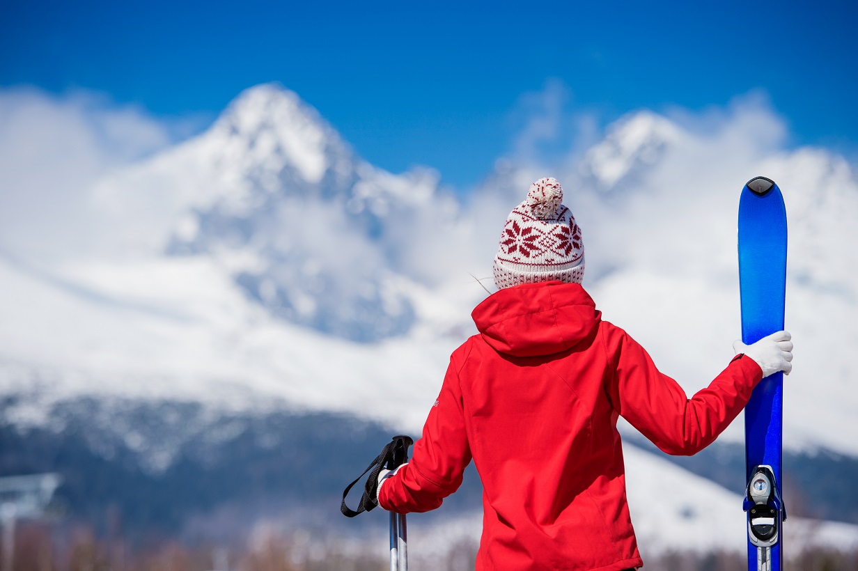 A woman holds skis looking at snowy mountains