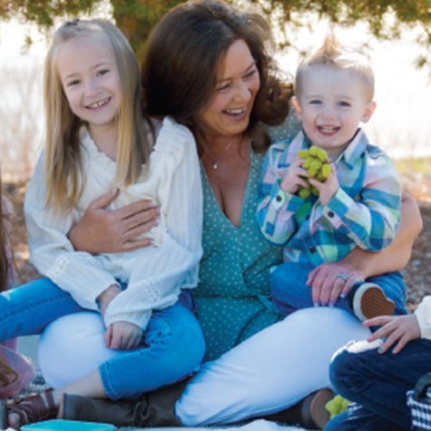 Pam Lundeen sitting in the park with 4 of her grandchildren surrounding her.
