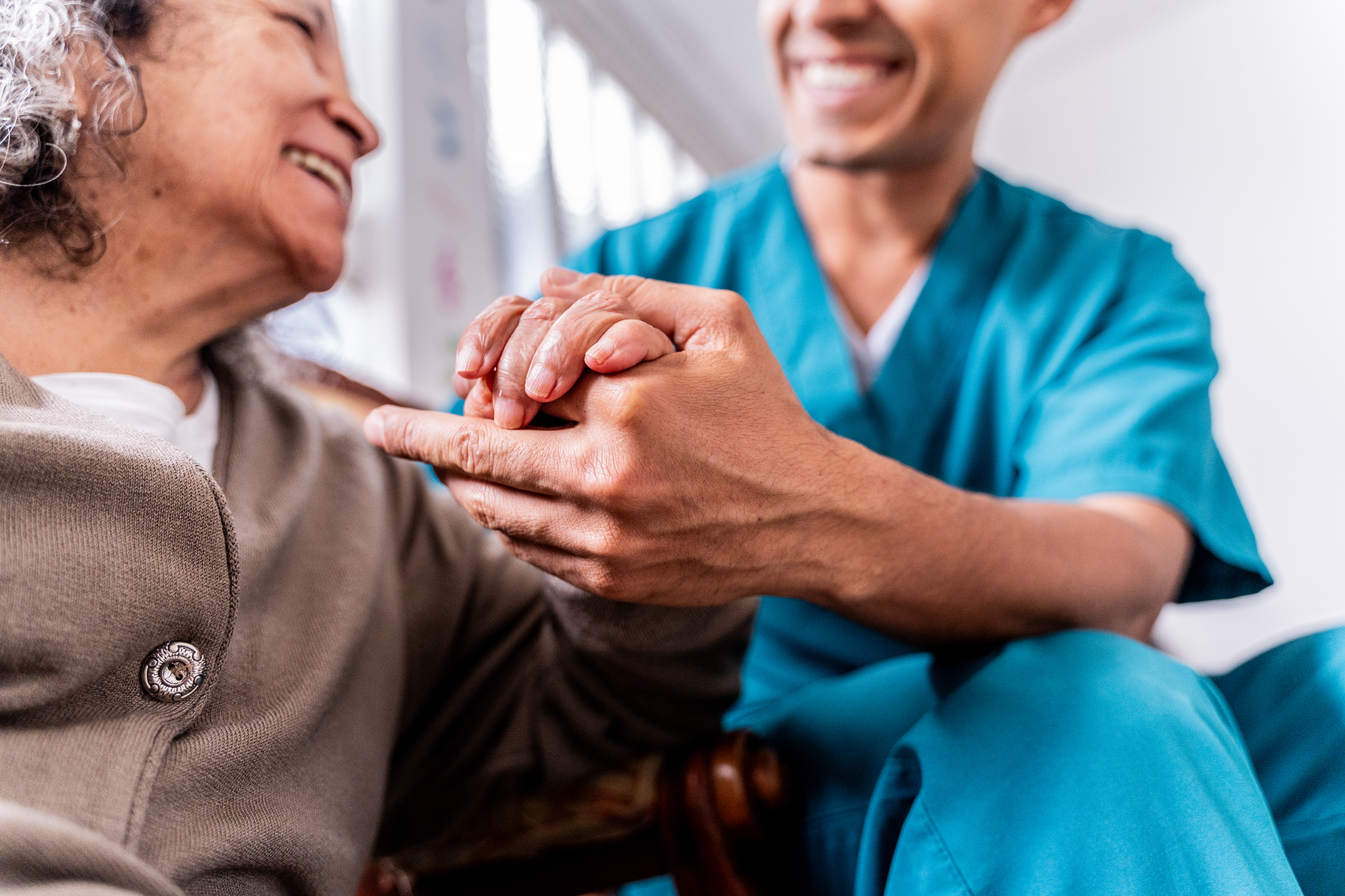 A woman smiles while a home healthcare provider holds her hand.