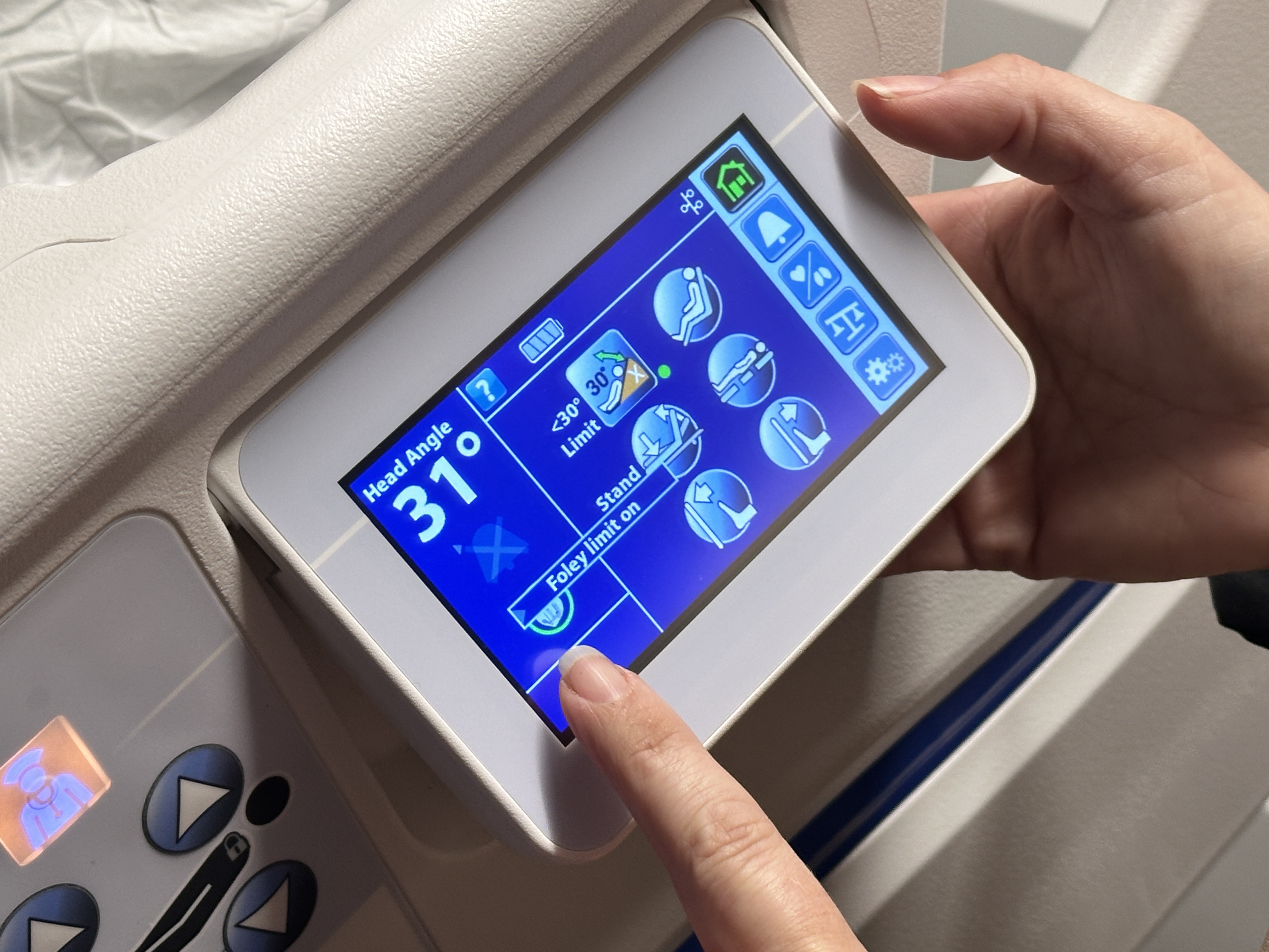 Person pointing to a touchscreen on a patient bed.