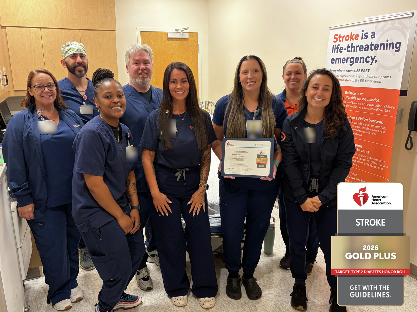 Group of healthcare staff in a hospital treatment room posing with an American Heart Association Stroke Gold Plus award certificate. A stroke awareness banner is displayed in the background, and a 2026 Gold Plus recognition badge appears on the image.