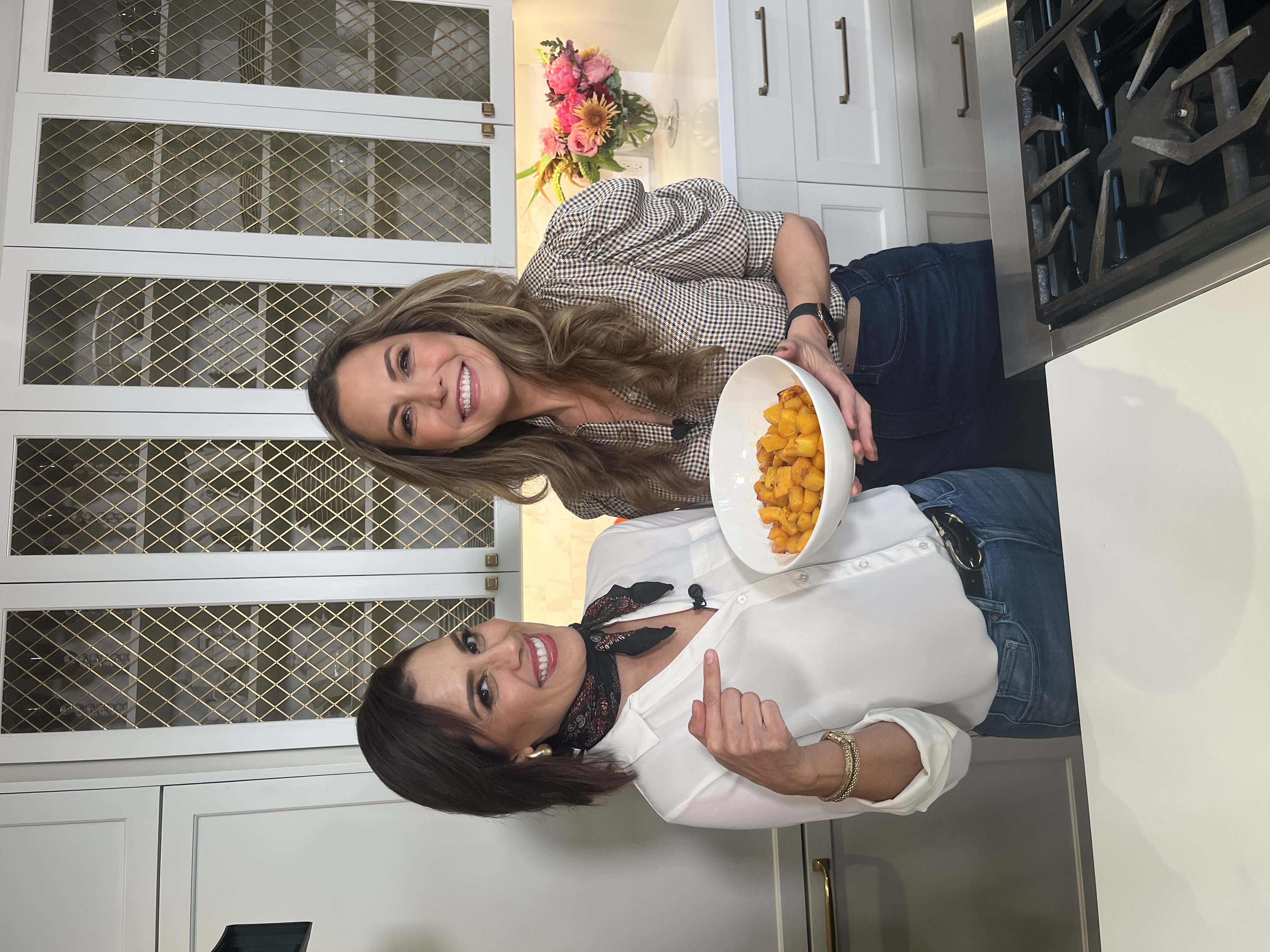 Claudia Zapata-Elliott and Brenda Macias smiling while holding a colorful holiday dish.