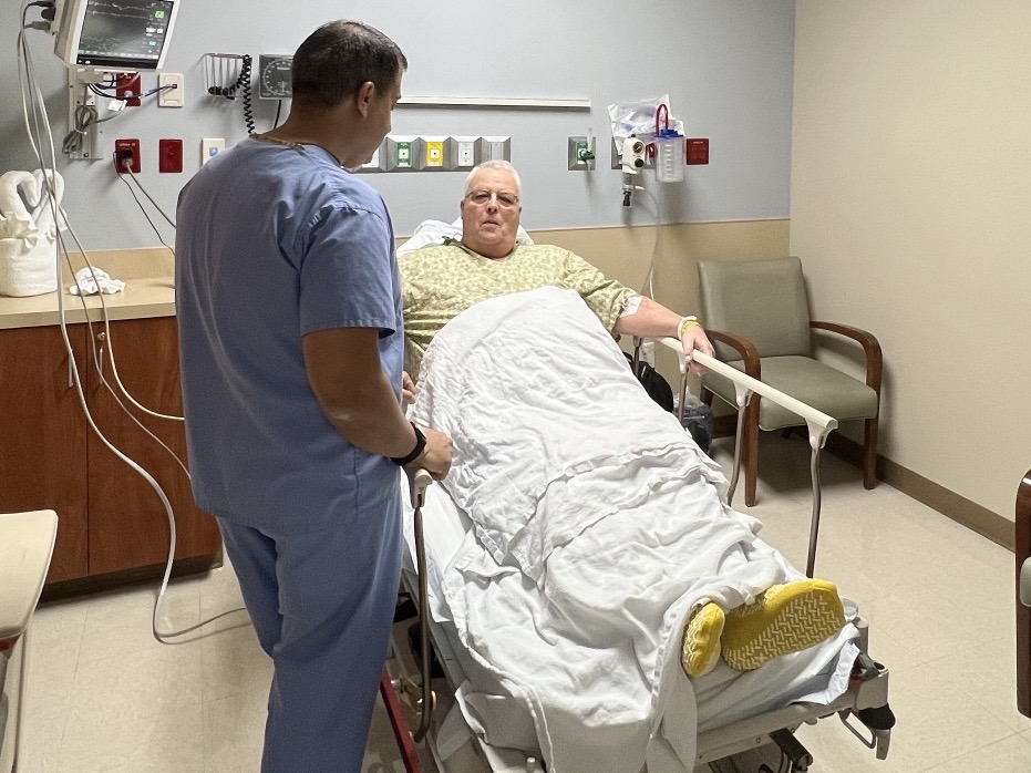 Calvin Nesset in hospital bed with nurse nearby