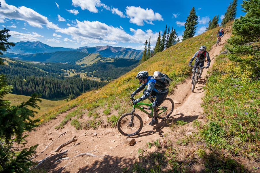 Three mountain bikers descending a switchback on a steep section of the "403" singletrack in the Rocky Mountains.