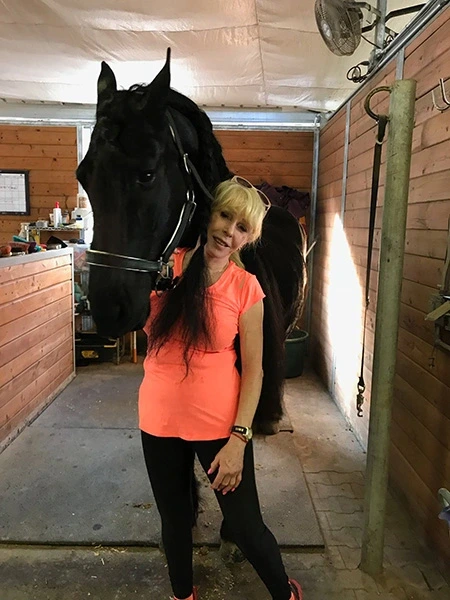 Registered Nurse, Marlene L., poses with her horse, Keimpe, in a stable.