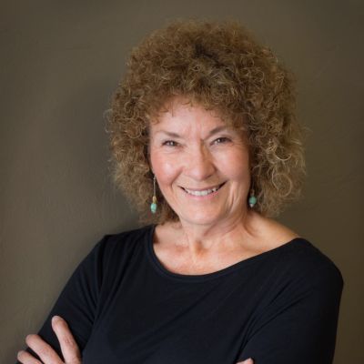 Lynette Loughton, smiling and crossing her arms, wearing a black long-sleeve shirt and earrings.