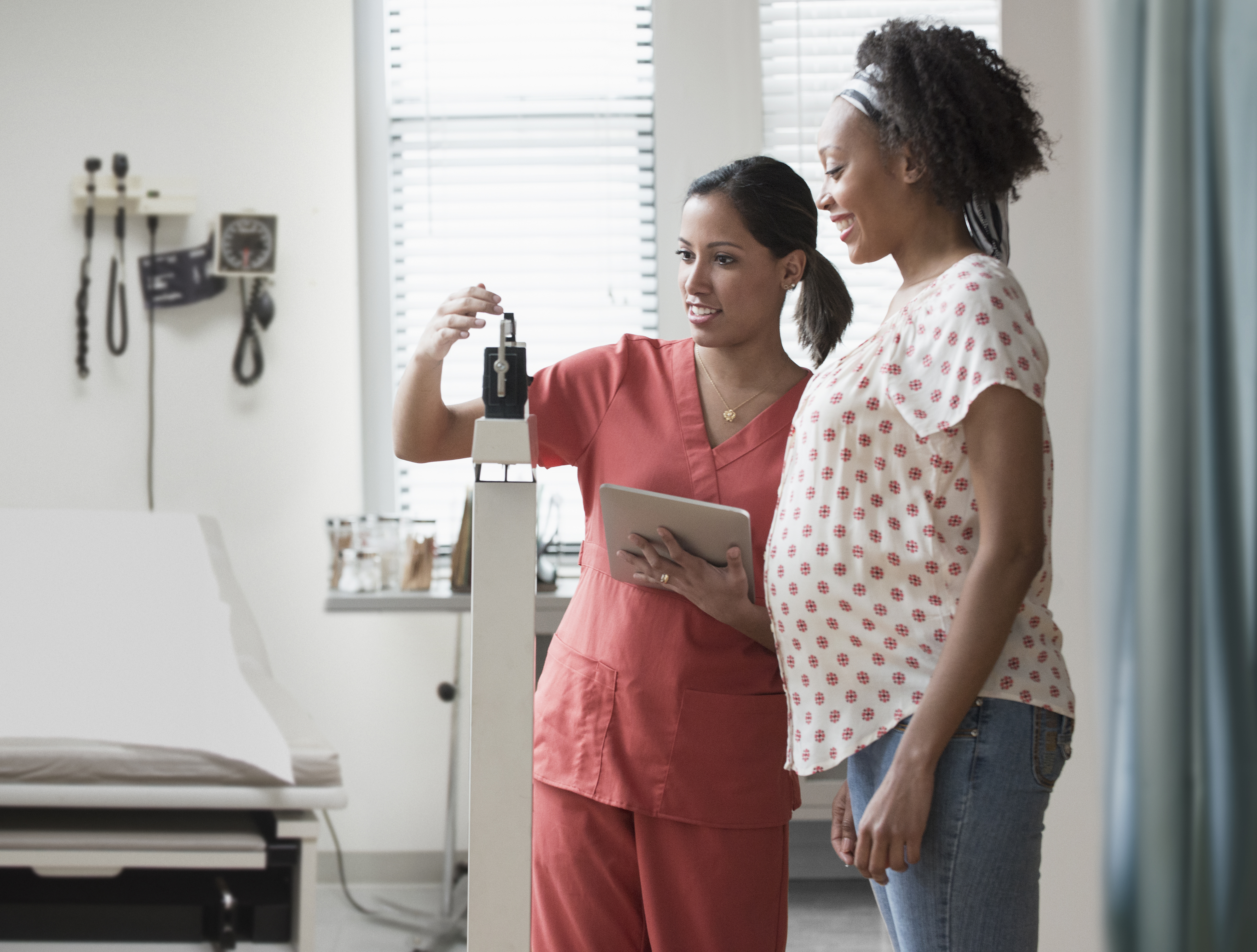 Nurse weighing pregnant woman in hospital room.