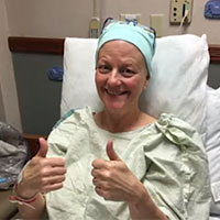 Jeanne sitting in her hospital bed, smiling and giving a thumbs-up.