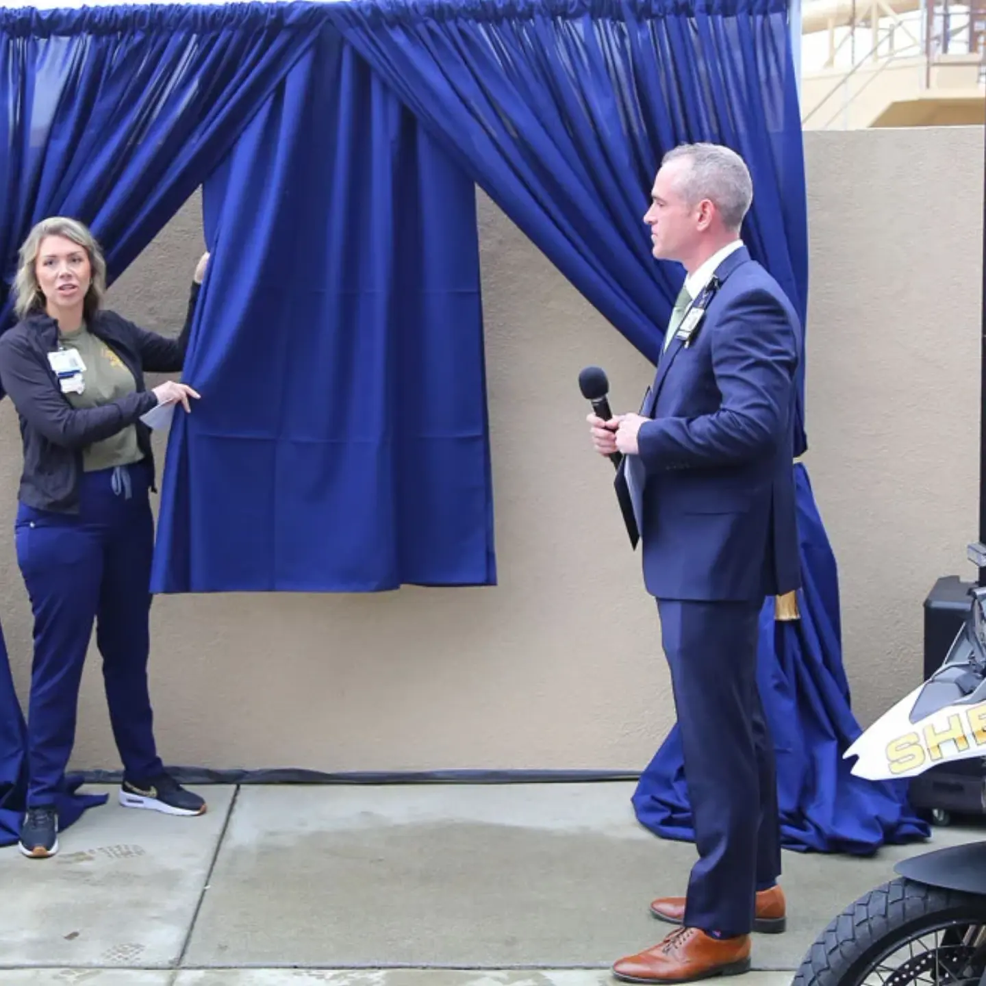 Lacey Page pulls a curtain down that is covering a plaque dedicating a parking space at Riverside Community Hospital to Timothy Corlew.