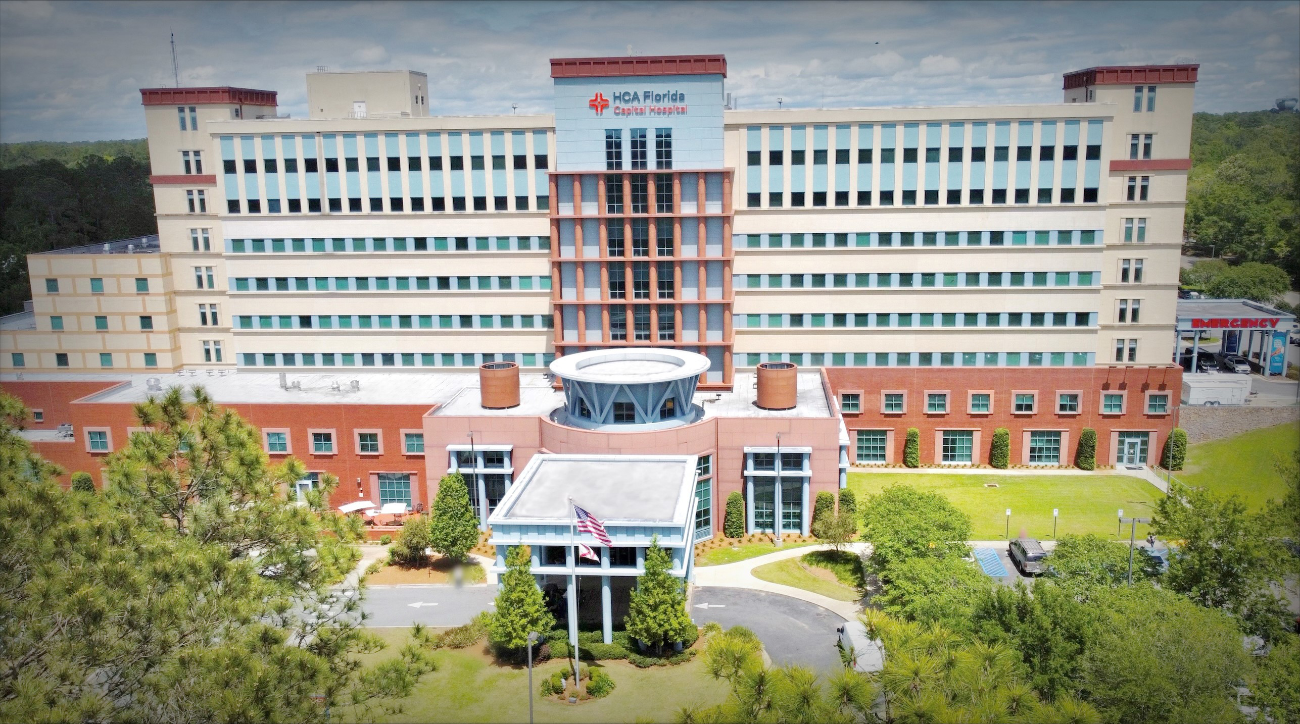 Capital Hospital photograph taken from a drone. Trees and a green lawn and an American flag on a flagpole in front of the entryway overhang.