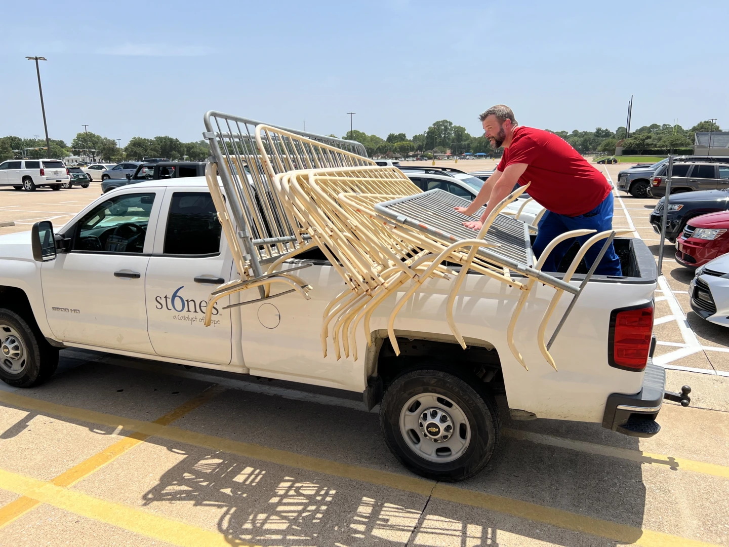 A volunteer from Medical City North Hills, wearing a red T-shirt, loads items into a 6 Stones pickup truck to help set up for a back-to-school event.