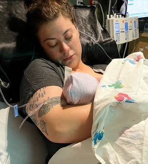 Cameron Jennings rests in her hospital bed, holding her newborn son Will who is wrapped in a hospital blanket.