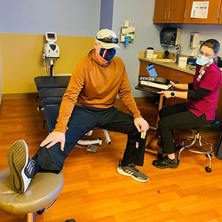Long-haul COVID-19 symptom patient, John Cashin, demonstrating the mobility of his right leg to a nurse during a treatment evaluation.