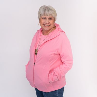 Julie, an oncology patient at West Valley Medical Center, poses in a pink shirt and sweatshirt against a white backdrop.