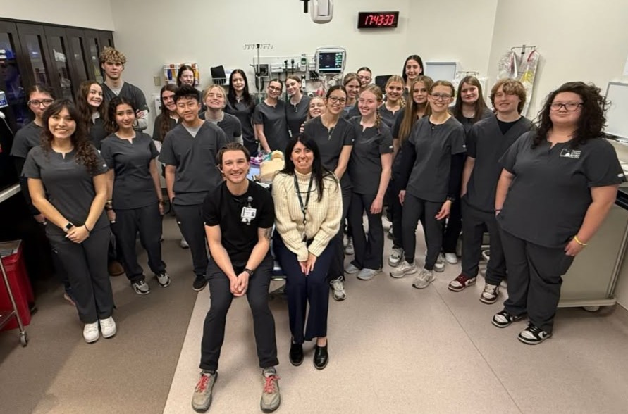 A group of AHEC Medical Scholars students and instructors wearing scrubs pose in a clinical simulation lab at HCA Healthcare's Center for Clinical Advancement in Draper.