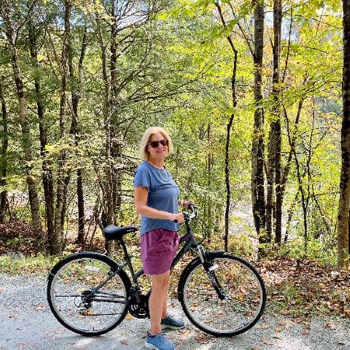 Carolyn poses with her bicycle, while on a trail in a wooded area.