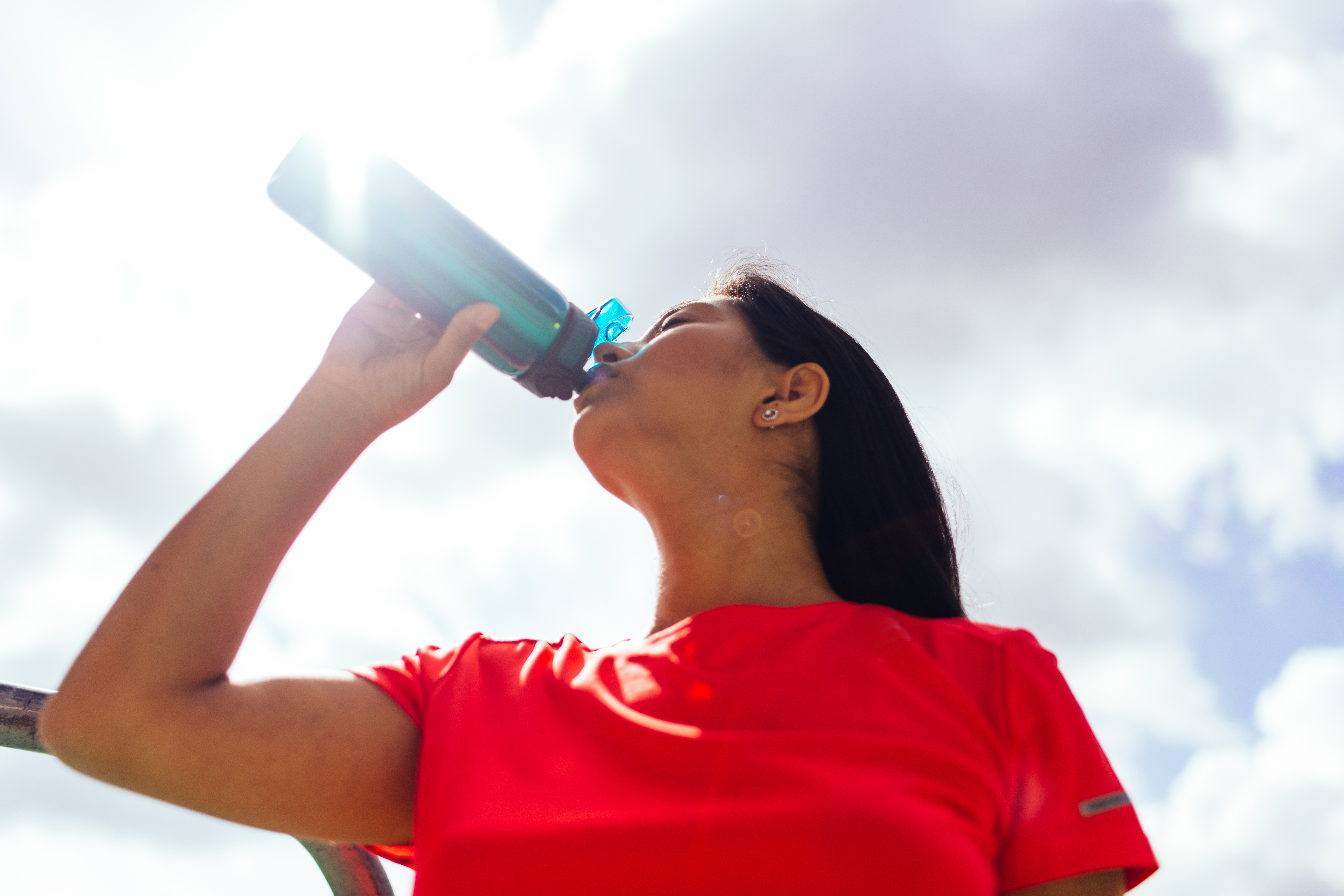 Woman standing outdoors, drinking from a water bottle.