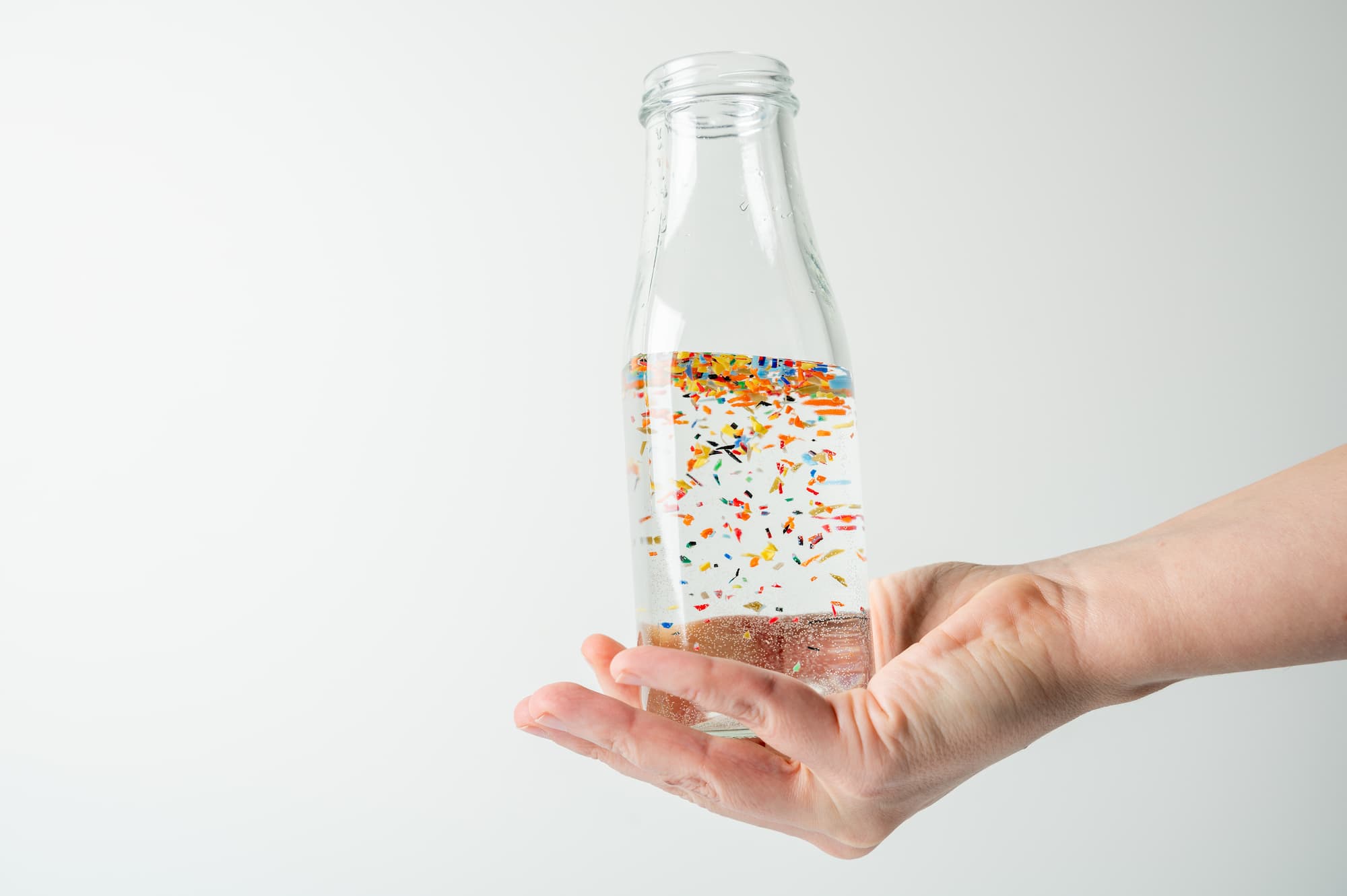 A person holds a small bottle of water with microplastics floating inside it.