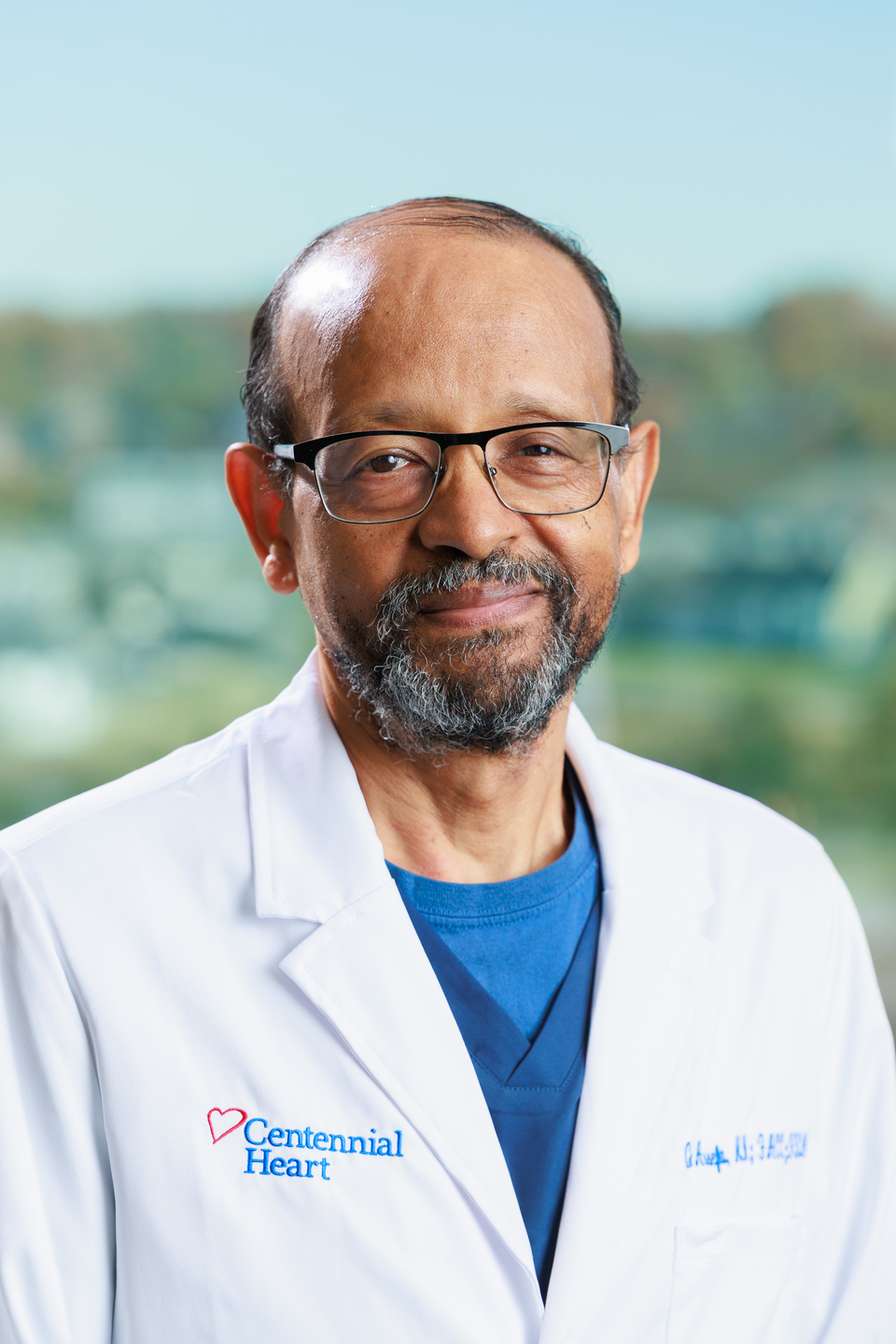 Portrait of a Centennial Heart cardiologist in a white lab coat standing in front of large office windows.
