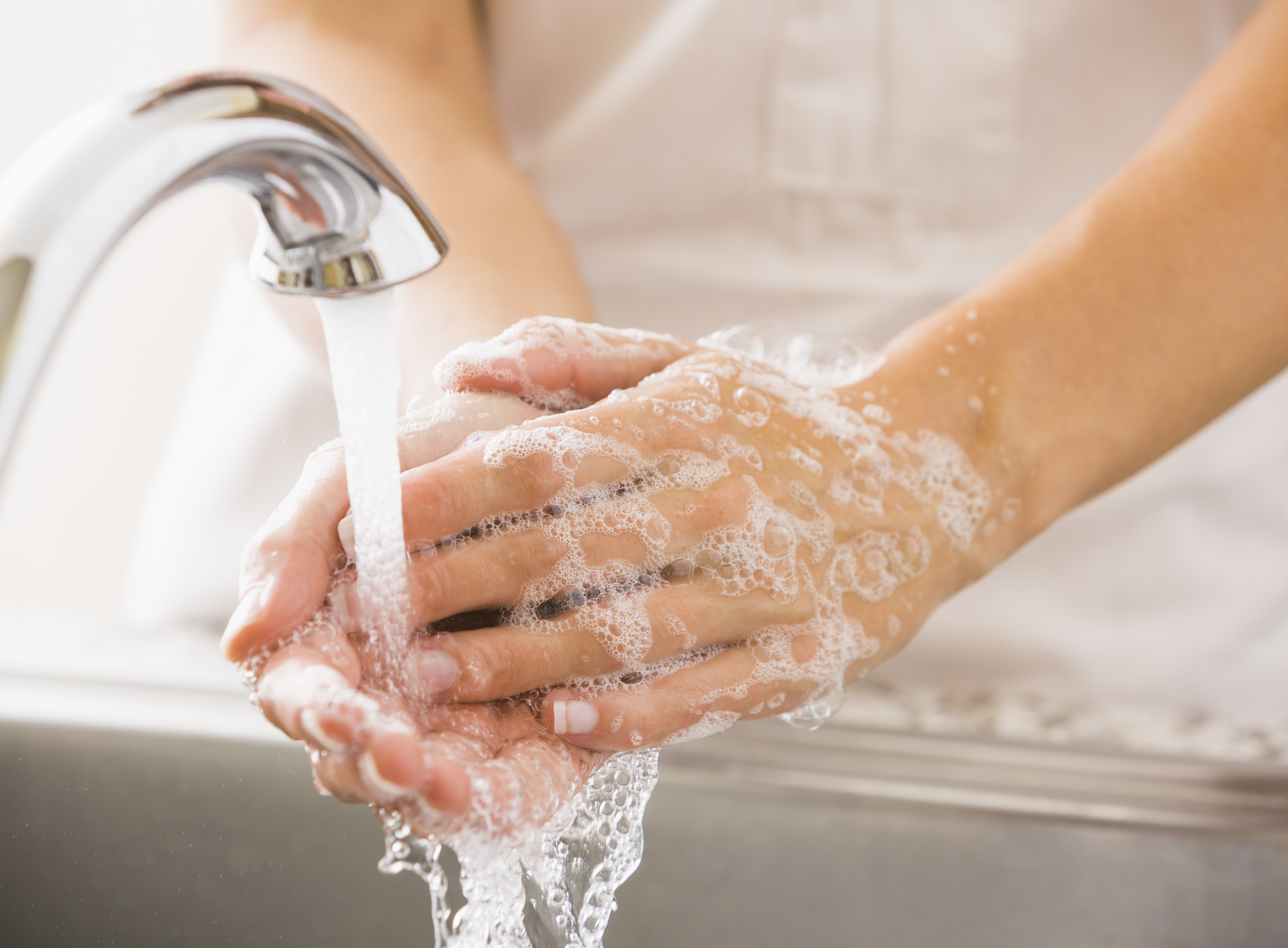  A person's hand being washed under a running kitchen faucet.