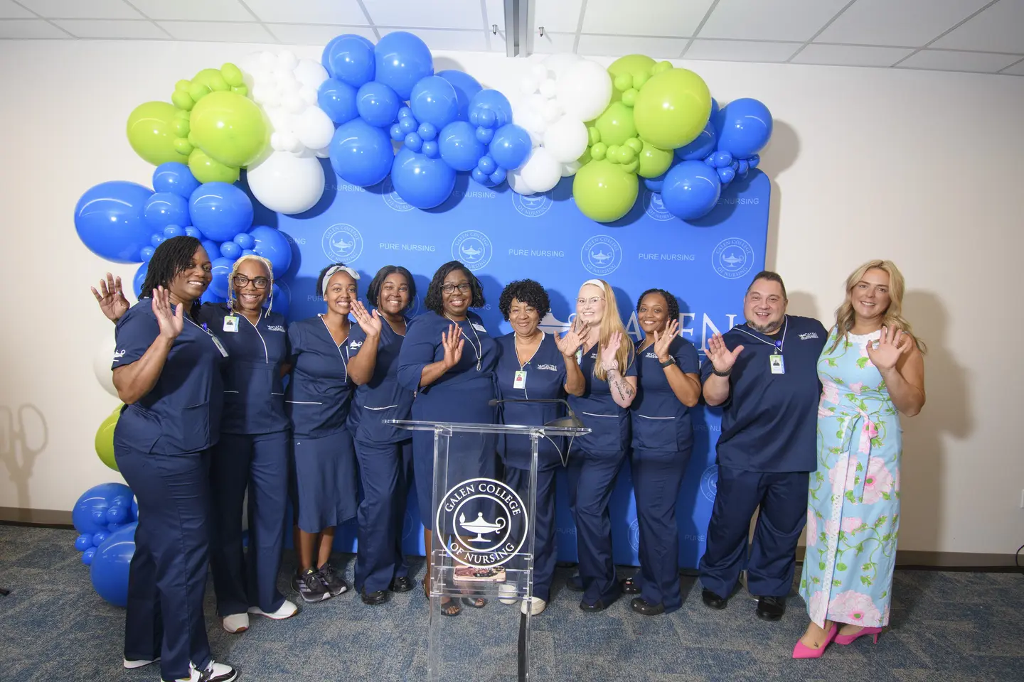 Galen College nurse students and leaders pose at grand opening with podium and blue, white, and green balloons on blue backdrop