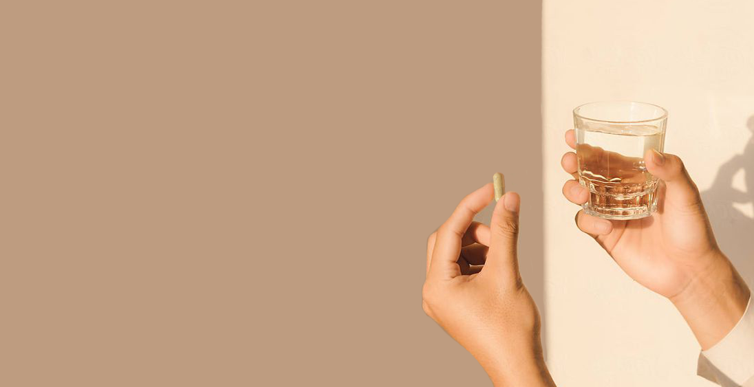 A person holds up a vitamin pill and a glass of water in the sun, casting shadows on the wall.