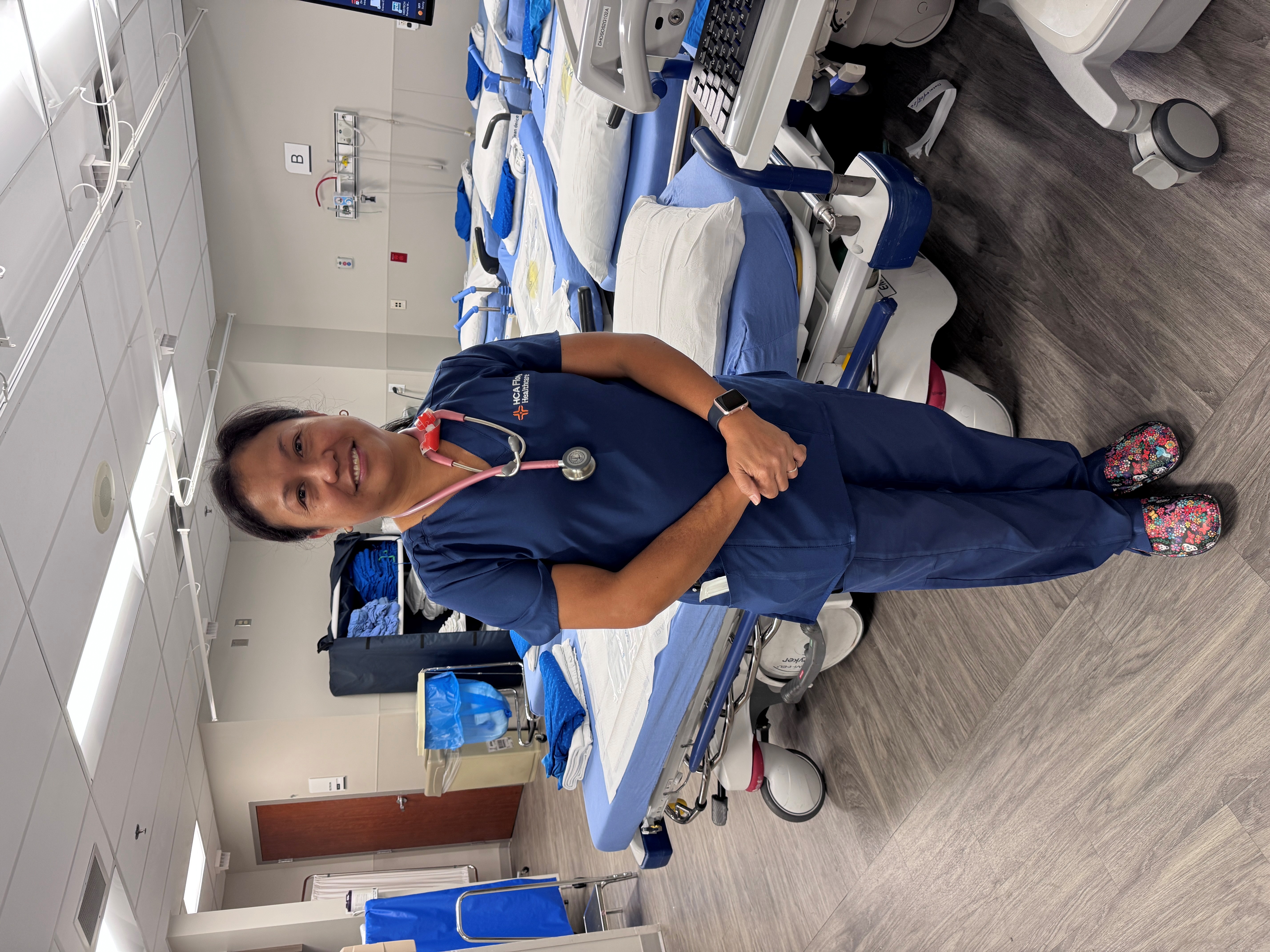 Nurse wearing scrubs standing next to a hospital bed