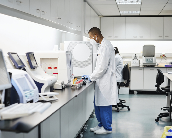 A medical lab professional wearing a face mask and working at a counter with lab equipment.