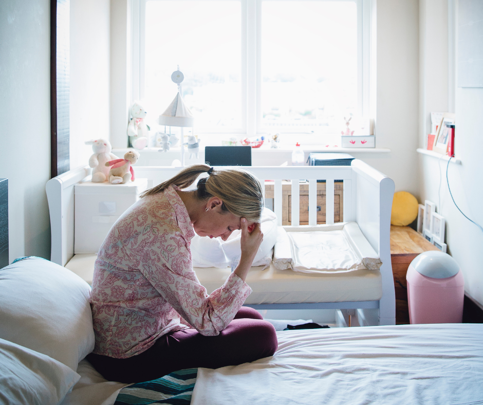 sad mother sitting on bed next to crib
